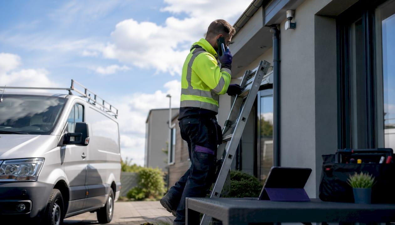 Electrician using smartphone and tablet on ladder