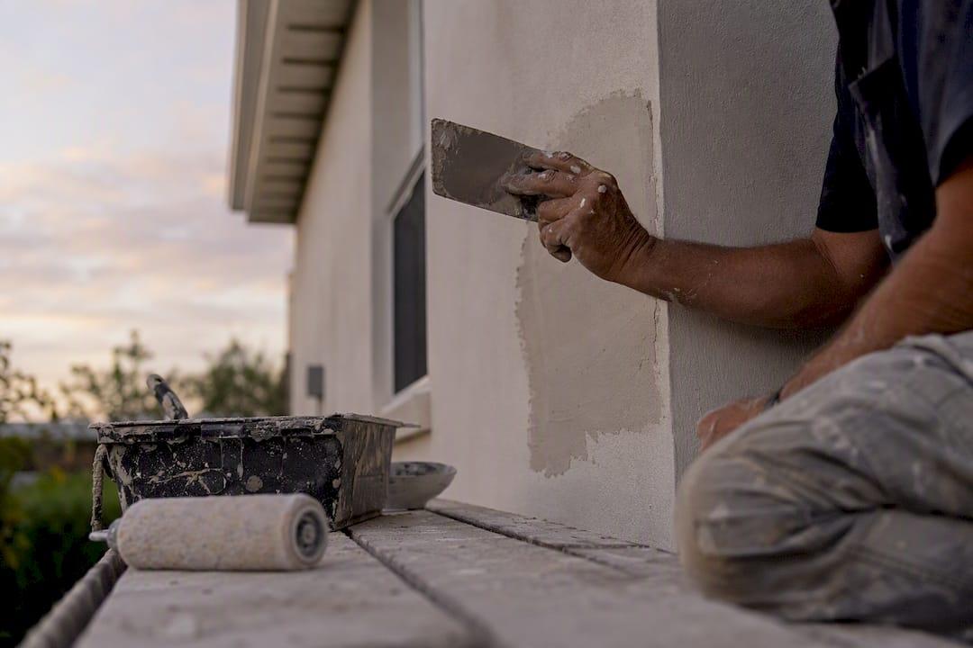 Hands painting repaired wall patch on building